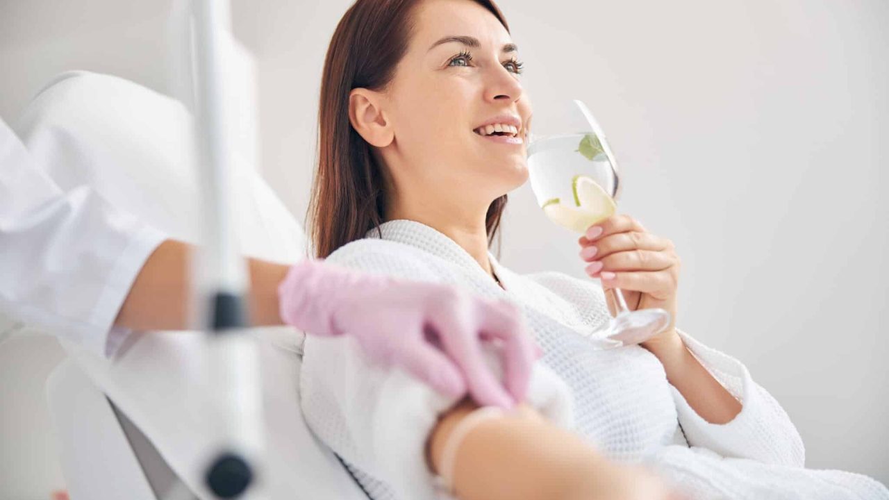 A woman drinking water as she is getting IV hydration Therapy