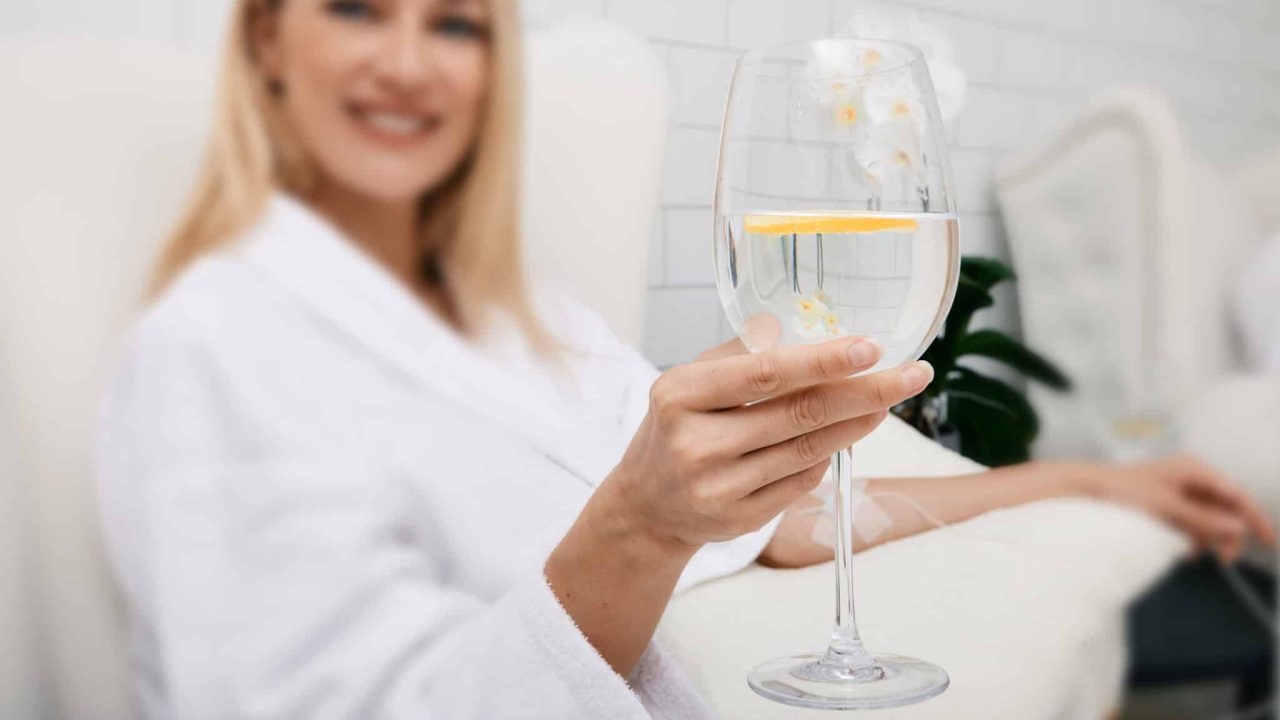 Beautiful woman with glass of refreshing lime drink during intravenous detox therapy with IV drip Infusion. Detox treatments at spa