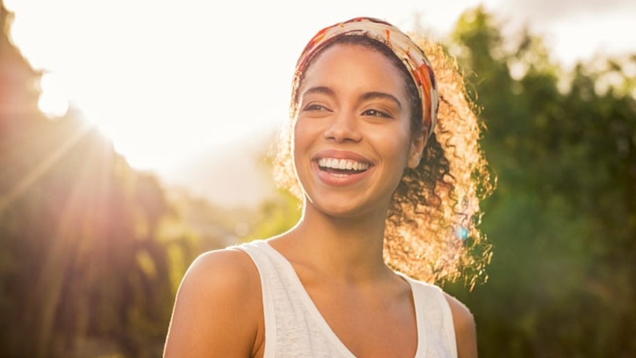 Portrait of beautiful african american woman smiling and looking away at park during sunset. Outdoor portrait of a smiling black girl. Happy cheerful girl laughing at park with colored hair band.
